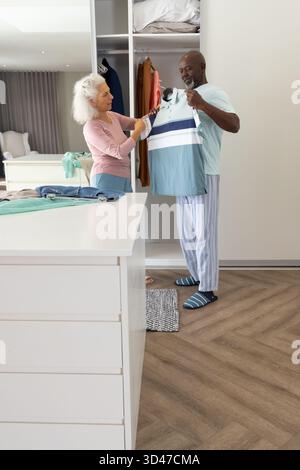 Una coppia senior sta esaminando una polo a righe nel moderno armadio grigio chiaro della camera da letto, spazio fotocopie Foto Stock
