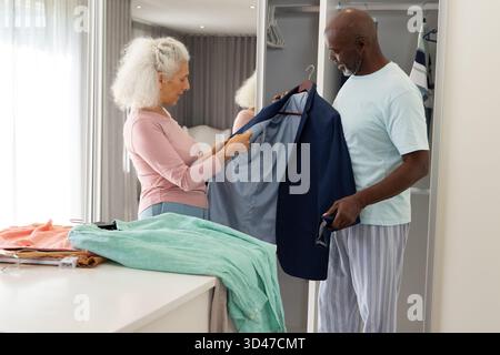 Diverse coppie anziane che esaminano il blazer navy nell'area spogliatoio della camera da letto, con abiti piegati Foto Stock