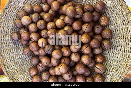 Nocciole di macadamia intere in un cestino intrecciato su sfondo di legno Foto Stock