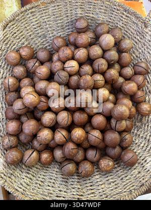 Nocciole di macadamia intere in un cestino intrecciato su sfondo di legno Foto Stock