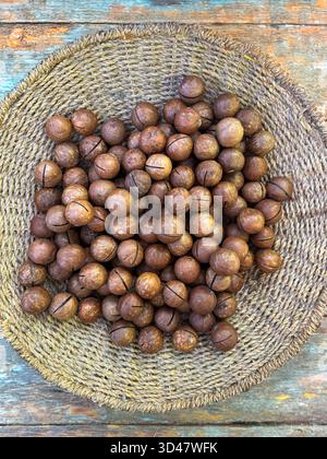 Nocciole di macadamia intere in un cestino intrecciato su sfondo di legno Foto Stock