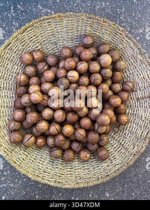 Nocciole di macadamia intere in un cestino intrecciato su sfondo di legno Foto Stock