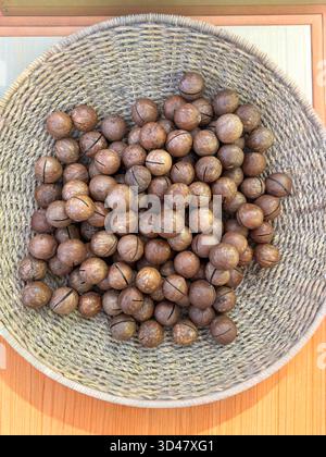 Nocciole di macadamia intere in un cestino intrecciato su sfondo di legno Foto Stock