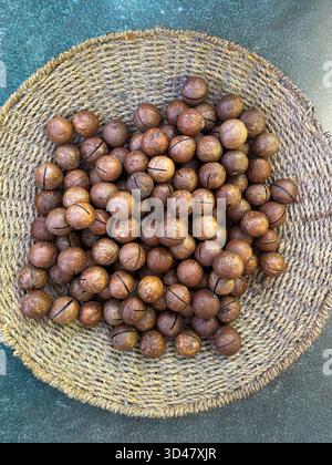 Nocciole di macadamia intere in un cestino intrecciato su sfondo di legno Foto Stock