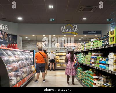 Cremona, Italia - 15 agosto 2025 clienti che cercano prodotti freschi e prodotti da forno in una moderna navata di supermercati con abbondanti esposizioni di frutta Foto Stock