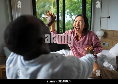 Giovani coppie diverse che sorridono gioiosamente insieme nel loro luminoso soggiorno, indossando abiti casual Foto Stock