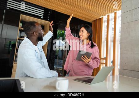 Felice coppia multietnica che utilizza un notebook, acquista online con le vendite, gioca insieme Foto Stock