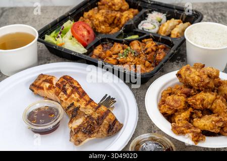 Pasto in stile familiare a tavola con abbondante pollo al sesamo, scatola bento di pollo piccante e colletto di salmone per un gruppo numeroso. Foto Stock