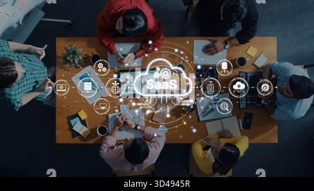 Un team diversificato di professionisti collabora alle soluzioni SaaS in uno spazio di lavoro moderno. Le icone digitali illustrano i concetti di cloud computing e. Foto Stock