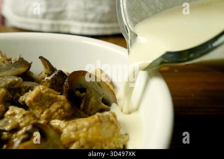 Pezzi di pollo fritti con funghi, nel latte in una tazza, pranzo aromatico Foto Stock