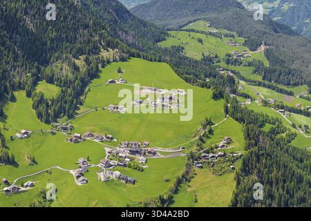 Vista aerea panoramica dell'idilliaco villaggio alpino circondato da lussureggianti colline verdi vicino alla Valle di Funes alle Dolomiti, Italia Foto Stock