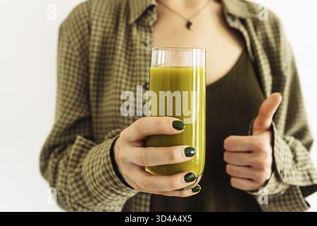 Mani ragazza con manicure verde, tenere in vetro fresco frullato mela, spinaci, sedano, kiwi. i vestiti della ragazza sono colore verde, parete della luce di fondo. Refreshi Foto Stock