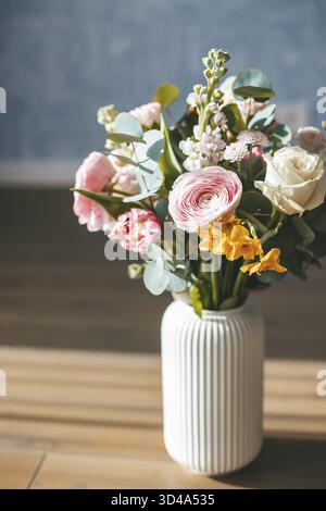 Un vivace e colorato bouquet di fiori assortiti in un vaso bianco su pavimento in legno Foto Stock