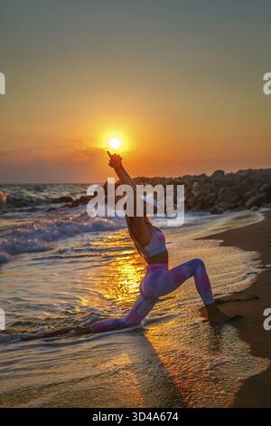 Bella donna bionda che pratica yoga in riva al mare durante il tramonto. Armonia interiore e cura del corpo Foto Stock