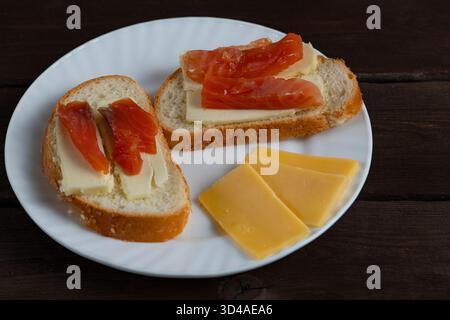 Panini fatti in casa con burro e fette di pesce rosso su piatto bianco con formaggio su fondo di legno scuro. Perfetto per la colazione o i temi del blog gastronomico Foto Stock