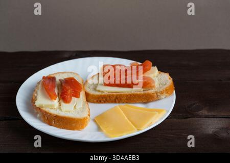 Panini fatti in casa con burro e fette di pesce rosso su piatto bianco con formaggio su fondo di legno scuro. Perfetto per la colazione o i temi del blog gastronomico Foto Stock