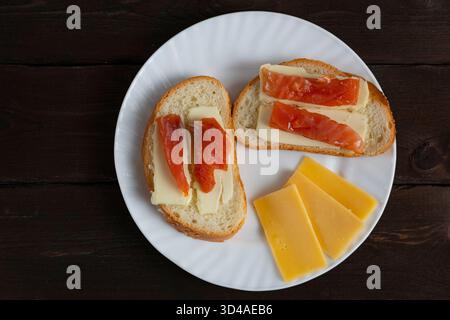 Panini fatti in casa con burro e fette di pesce rosso su piatto bianco con formaggio su fondo di legno scuro. Perfetto per la colazione o i temi del blog gastronomico Foto Stock