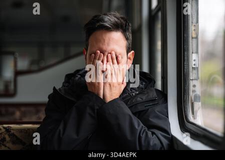 Uomo che copre il viso con le mani in un momento emotivo mentre è seduto all'interno del tram Foto Stock