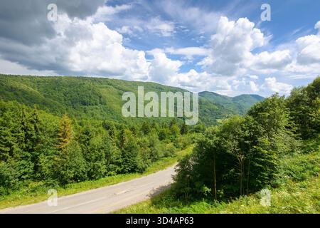 strada che attraversa il paesaggio montano in estate. vista panoramica dall'alto. verde paesaggio naturale in luce dappata sotto il cielo nuvoloso. splendida valle con pass Foto Stock