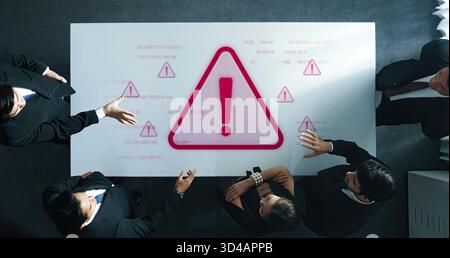 Vista dall'alto di un team aziendale riunito intorno a un tavolo con un simbolo di avviso evidenziato. Si impegnano in una discussione critica, analizzando i dati e. Foto Stock