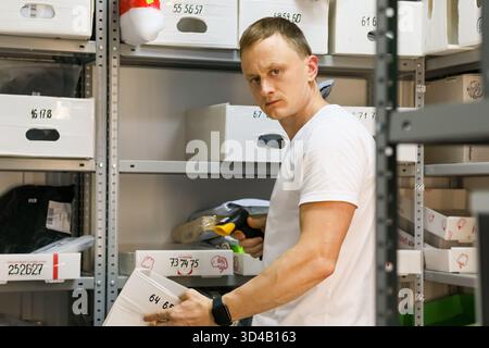 Lavoratore che estrae la scatola scansionata dallo scaffale nel magazzino di ritiro. Il dipendente tiene fermo il pacco e lo scanner durante il recupero dal rack nel magazzino Foto Stock