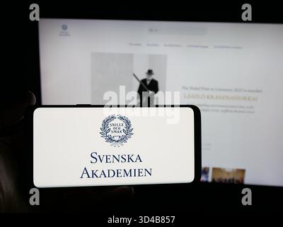 Stoccarda, Germania - 10-31-2025: Persona con smartphone con logo Svenska Akademien (Accademia svedese) sullo schermo davanti al sito Web. Foto Stock