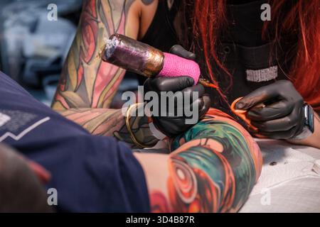 Dopo aver disegnato il disegno, un tatuatore utilizza una macchina per tatuaggi, un ago e le cartucce di inchiostro appropriate per inchiodare il disegno sulla parte del cliente Foto Stock