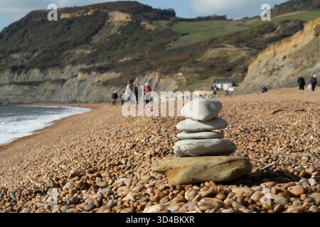 Un cairn è costruito sulla spiaggia di ciottoli di Seatown, Dorset, Regno Unito, con le famiglie che si godono le scogliere della Jurassic Coast. Foto Stock