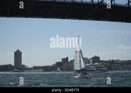Barca a vela nelle acque instabili del porto di Sydney sotto l'iconico Sydney Harbour Bridge, con lo skyline della città e altre barche sullo sfondo. Foto Stock