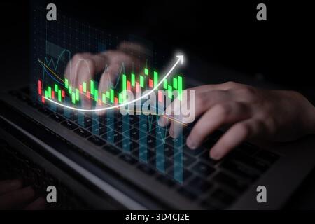 Una vista ravvicinata della digitazione manuale su un notebook con vivaci grafici del mercato azionario visualizzati sullo schermo, che simboleggia il mondo dinamico della finanza Foto Stock