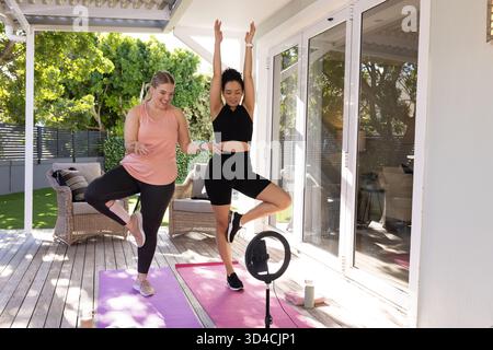 Allenati con diverse amiche in posa sugli alberi sul ponte di legno, con colorati tappetini per yoga Foto Stock