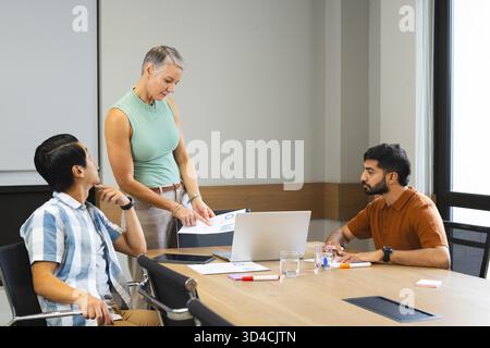 Diversi colleghi che discutono di carte stampate nella moderna sala conferenze, con laptop color argento Foto Stock