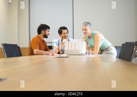 Discutere di diversi colleghi intorno al computer portatile nella sala conferenze dell'ufficio, con notebook e pennarelli Foto Stock