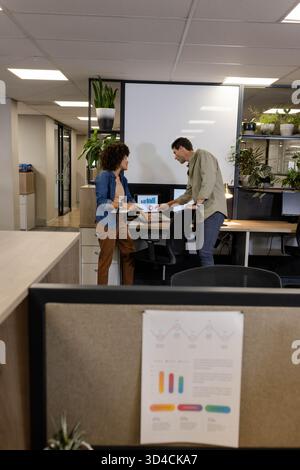 Revisione di diversi colleghi che analizzano grafici a barre e grafici a torta in ufficio, con tablet e notebook Foto Stock