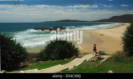 Una donna con due cani cammina lungo un sentiero sinuoso fino alla spiaggia di sabbia bianca di South West Rocks NSW Foto Stock