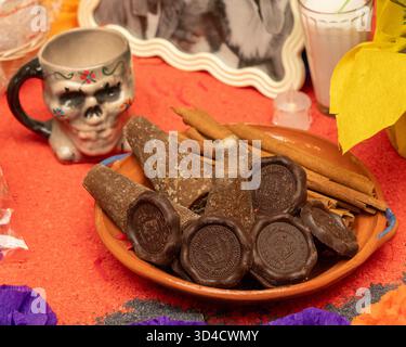 Una ciotola di caramelle al cioccolato siede su un tavolo con una tazza teschio e una foto di una persona. La tradizione messicana del giorno dei morti, offerte, cibo, colori, tedesco Foto Stock