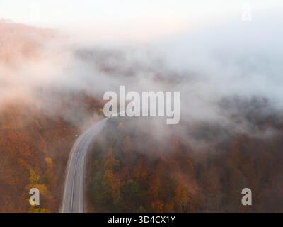 Colpo di droni dall'alto di una strada curva che scompare in nuvole basse e nebbia Foto Stock