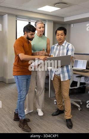 Collaborazione con colleghi diversi che analizzano i dati in un ufficio open space, con stampe su notebook e carta Foto Stock