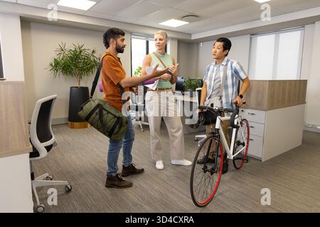 Parlare di colleghi diversi in un ufficio open space, con borsone verde e bicicletta da strada Foto Stock