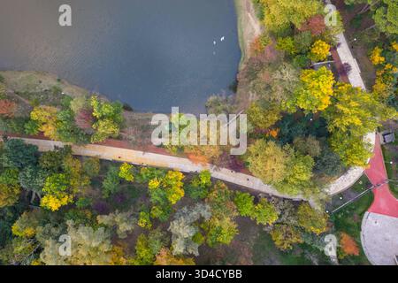 Vista aerea dall'alto verso il basso del Parco del Lago di Tirana in autunno, mostrando alberi colorati, sentieri e parte del lago calmo. Foto Stock
