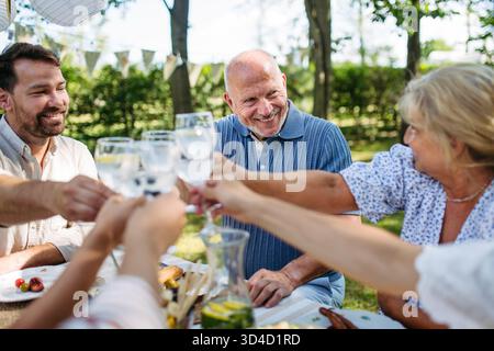 Brindisi multigenerazionali in famiglia durante una festa al barbecue all'aperto. Foto Stock