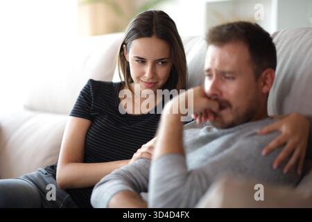 Falsa cattiva amica felice di vedere la sua triste compagna su un divano a casa Foto Stock