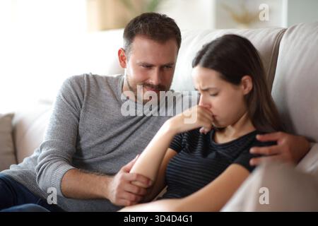Falso cattivo amico felice di vedere il suo triste compagno su un divano a casa Foto Stock