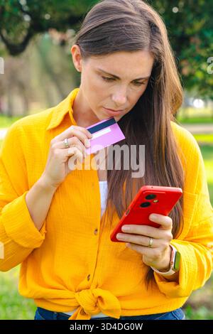 Giovane donna che fa shopping online con carta di credito e smartphone all'aperto Foto Stock