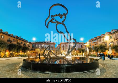 Vista al crepuscolo di una moderna scultura in metallo dell'artista Valerio Berruti su una piazza della città, con un albero di Natale illuminato sullo sfondo ad Alba, Italia. Foto Stock