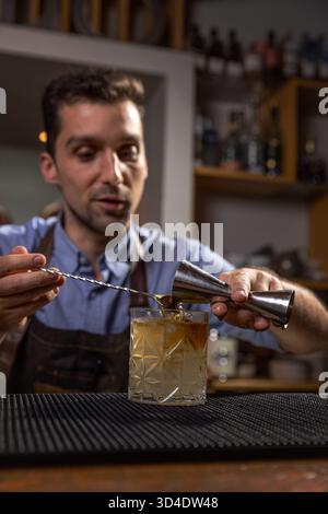 Il barista versa il liquido nel bicchiere da cocktail con il jigger Foto Stock