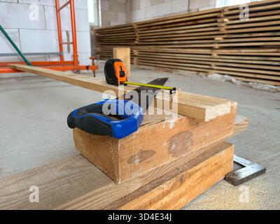 Un metro a nastro, una matita e una sega a mano giacciono su una tavola. Industria edile. Utensili da costruzione e strumenti di misurazione. Foto Stock