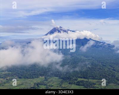 Vista aerea del Monte Merapi avvolta da nuvole eteree, la sua vetta baciata dal cielo, una maestosa sentinella del potere grezzo della natura, Klaten Regency, CE Foto Stock
