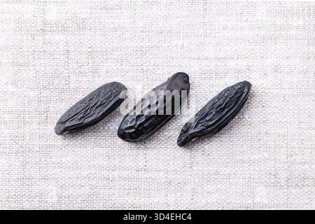 Tre fagioli tonka, primo piano, dall'alto, su lino. Noti anche come fagioli di tonchino o tonchino, semi neri e rugosi dell'albero Dipteryx odorata. Foto Stock