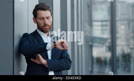 Uomo d'affari maturo caucasico che guarda un orologio da polso in città uomo d'affari sorridente datore di lavoro maschio adulto in attesa di incontrare un manager felice imprenditore Foto Stock